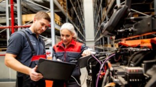 Dva servisna tehnika podjetja Linde Material Handling gledata v prenosni računalnik ob viličarju.
