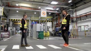 V skladišču se srečata dva zaposlena, ki nosita zaščitni jopič Linde Secure Distance Vest in zvočni opozorilnik Linde Distance Beeper.