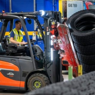 Zaposleni v podjetju Michelin Tyre PLC z objemko za pnevmatike, nameščeno na viličarju, zgrabi kup pnevmatik.