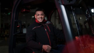 Delavec podjetja Linde Material Handling sedi v vozilu za talni transport in se nasmehne v kamero.