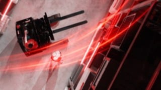 Pogled na regalni viličar Linde MH Ri16 z rdečimi svetlobnimi sledmi iz ptičje perspektive, ob njem pa oseba, ki izvaja stojo na rokah.
