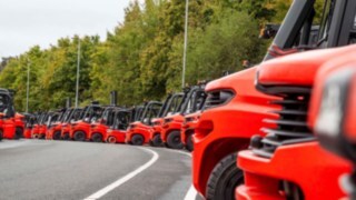 Na parkirišču je v vrsti parkiranih veliko viličarjev podjetja Linde Material Handling.